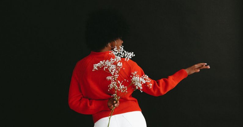 Romantic Getaway - Back view of sensual black woman in white denim and white red sweater holding Gypsophila flower behind back posing on black backdrop