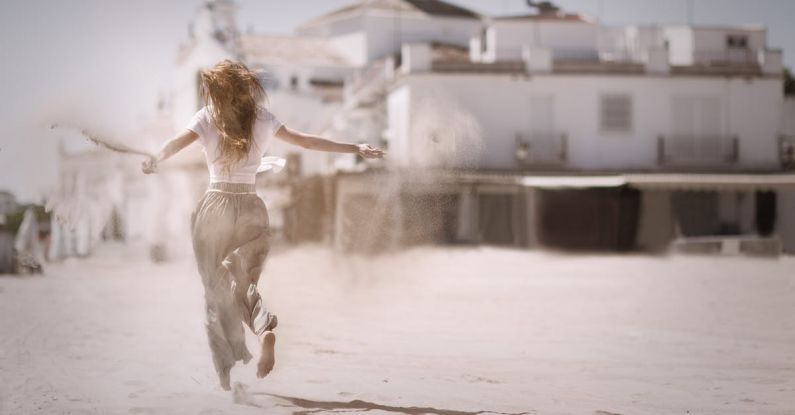 Beach Festivals - Woman Running on Sand Near White Concrete Building