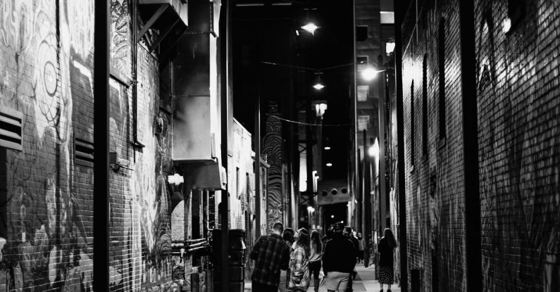 Late Night Activities - People walking on street with brick buildings with graffiti
